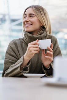 Porträt einer lächelnden jungen Frau, die eine Tasse Kaffee hält und wegschaut - DIGF08974