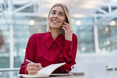 Smiling young businesswoman with notebook on the phone - DIGF08980