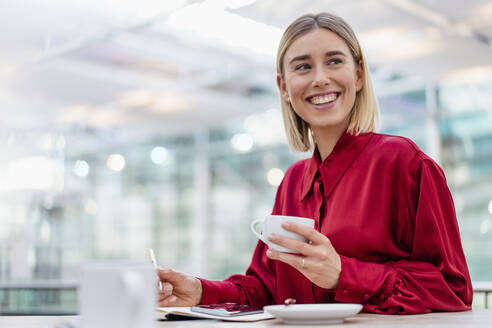 Happy young businesswoman taking notes in a cafe - DIGF08984