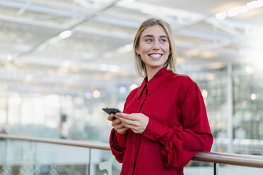 Lächelnde junge Geschäftsfrau an einem Geländer stehend mit Mobiltelefon - DIGF08992