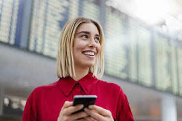 Lächelnde junge Geschäftsfrau mit Handy bei der Ankunft Abflug Bord auf dem Flughafen - DIGF08997