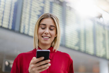 Lächelnde junge Geschäftsfrau mit Handy bei der Ankunft Abflug Bord auf dem Flughafen - DIGF08998