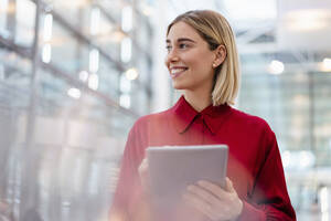 Smiling young businesswoman wearing red shirt using tablet - DIGF09005