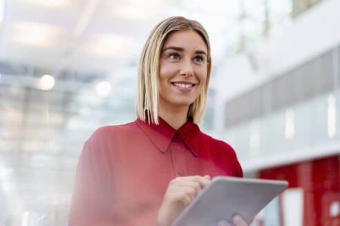 Smiling young businesswoman wearing red shirt using tablet - DIGF09007