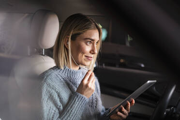 Smiling young woman with tablet and earphones in a car - DIGF09022