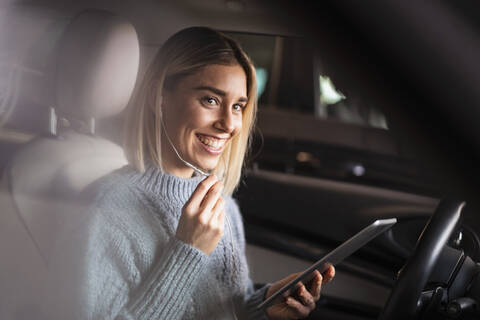 Glückliche junge Frau mit Tablet und Kopfhörern in einem Auto, lizenzfreies Stockfoto