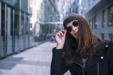 Porträt einer Frau mit Sonnenbrille, die in die Kamera schaut, Hand auf der Brille - DHEF00005