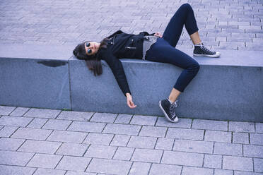 Woman with sunglasses lying on concrete bench - DHEF00007