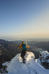 Bergsteiger, der den Gipfel eines verschneiten Berges erreicht und die Aussicht genießt, Lecco, Italien - MCVF00094