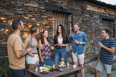Eine Gruppe von Freunden unterhält sich und trinkt im Freien an einem Steinhaus - MPPF00360