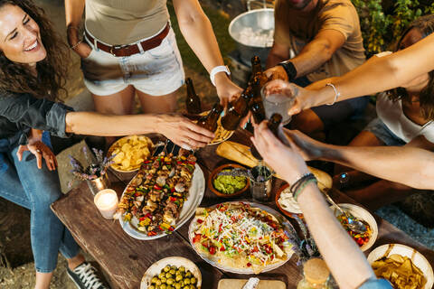 Glückliche Freunde stoßen bei einem Abendessen im Freien mit Bierflaschen an, lizenzfreies Stockfoto