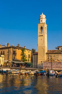 Italy, Province of Verona, Lazise, Boats moored in harbor in front of church bell tower - MHF00513