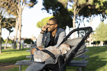 Berufstätiger Vater in einem Park, telefonierend, mit Baby im Kinderwagen - ERRF02215