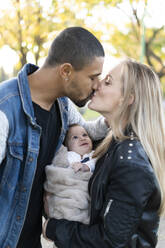 Glückliche Eltern, die sich im Park küssen, mit ihrem kleinen Sohn zwischen ihnen - ERRF02230