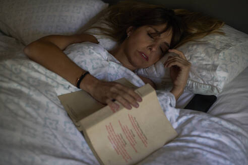 Frau schläft nach dem Lesen eines Buches im Bett ein - VEGF00991
