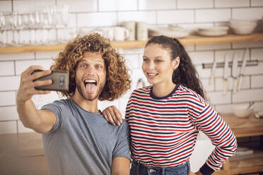 Playful couple taking a selfie in the kitchen at home - MCF00385