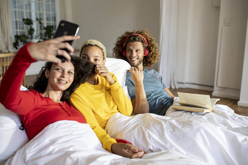 Glückliche Freunde, die sich zu Hause im Bett mit ihrem Smartphone entspannen - MCF00389