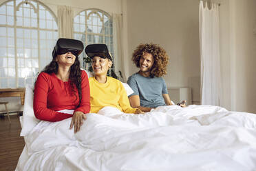 Happy friends having fun with VR glasses in bed at home - MCF00392