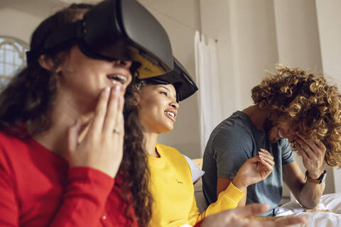 Happy friends having fun with VR glasses in bed at home stock photo