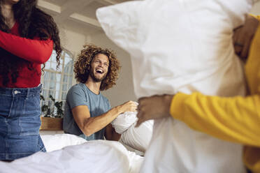 Happy friends having a pillow fight in bed at home - MCF00397