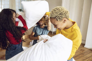 Happy friends having a pillow fight in bed at home - MCF00398