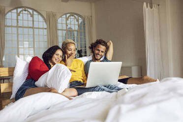 Glückliche Freunde, die sich zu Hause im Bett entspannen und einen Film auf dem Laptop ansehen - MCF00400