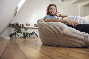 Young man relaxing in beanbag at home listening to music - MCF00403