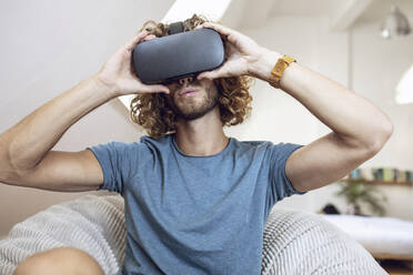 Young man wearing VR glasses at home - MCF00404