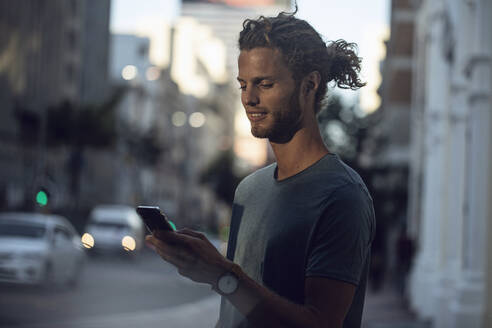 Selbstbewusster junger Mann mit Smartphone in der Stadt - MCF00425