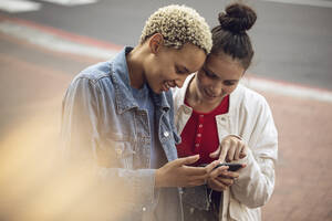 Zwei junge Frauen überprüfen ihr Smartphone in der Stadt - MCF00433
