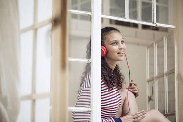 Happy young woman at the window listening to music - MCF00441