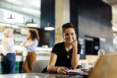 Junge Frau sitzt in einem Bistro und liest eine Zeitschrift, lizenzfreies Stockfoto