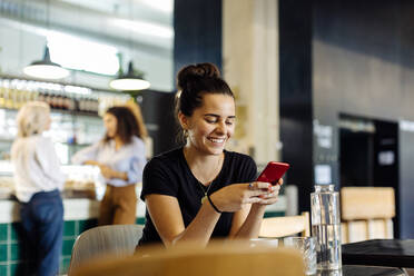 Young woman sitting in bistro, using smartphone - SODF00420