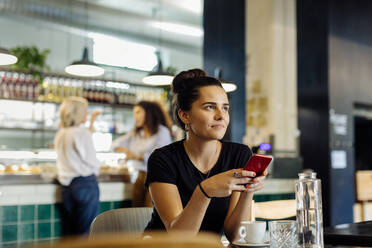 Junge Frau sitzt in einem Bistro und benutzt ihr Smartphone - SODF00421