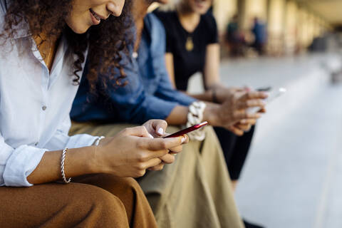 Drei Frauen sitzen auf einer Treppe in einer Reihe und benutzen Smartphones, lizenzfreies Stockfoto