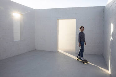 Kleines Mädchen in leerem Raum, stehend auf Skateboard - MCF00445