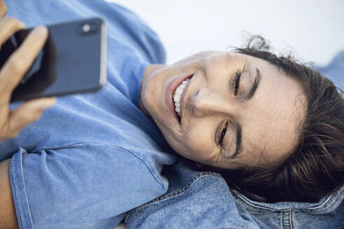 Young businesswoman relaxing, lying on wall, using smartphone - MCF00462