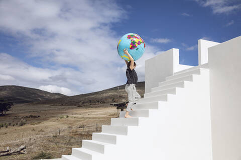 Kleines Mädchen auf weißer Treppe, trägt aufblasbaren Globus, lizenzfreies Stockfoto