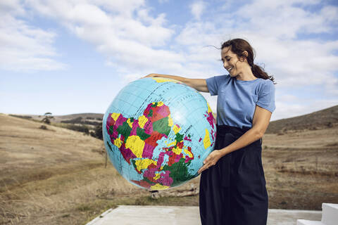 Ältere Frau hält aufblasbaren Globus, schaut zuversichtlich, lizenzfreies Stockfoto
