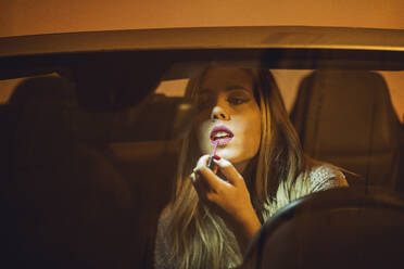 Portrait of blond woman in car applying lipstick - DLTSF00306