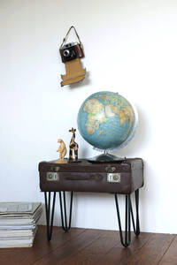 Globe and figurines standing on side table made of old suitcase, with old camera hanging on wall - GISF00479