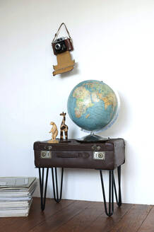 Globus und Figuren stehen auf einem Beistelltisch aus einem alten Koffer, an der Wand hängt eine alte Kamera - GISF00479