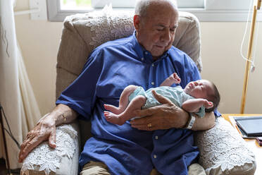 Großvater in einem Sessel sitzend, ein neugeborenes Baby haltend - GEMF03309