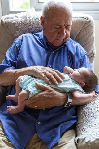 Grandfather sitting in an armchair holding a newborn baby stock photo