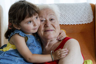 Lächelnde Großmutter, die ihre Enkelin zu Hause umarmt - GEMF03315