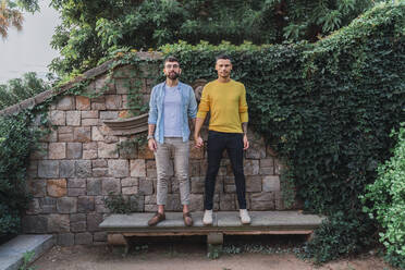 Portrait of gay couple standing hand in hand on stone bench - AFVF04327