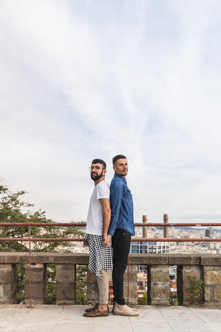 Porträt eines schwulen Paares, das Rücken an Rücken steht und sich an den Händen hält, Barcelona, Spanien, lizenzfreies Stockfoto