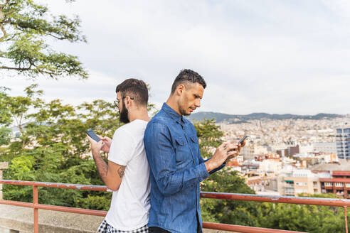 Schwules Paar steht Rücken an Rücken und benutzt Smartphones, Barcelona, Spanien - AFVF04340
