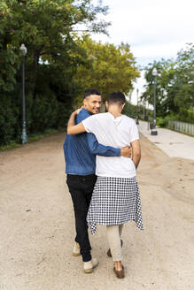 Rückenansicht eines glücklichen schwulen Paares, das Arm in Arm in einem Park spazieren geht, Barcelona, Spanien - AFVF04343