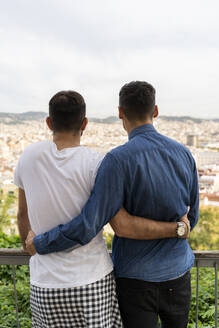 Rückenansicht eines schwulen Paares, das Arm in Arm auf die Stadt blickt, Barcelona, Spanien - AFVF04345